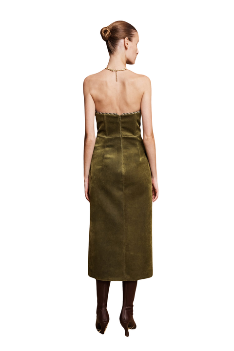 A woman shown from the back wearing a strapless olive green velvet midi dress with a structured corset-style bodice and scalloped neckline, paired with dark brown pointed-toe heels against a plain white background.