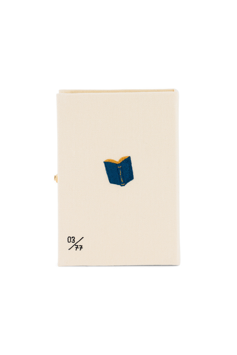 A cream-colored book clutch featuring a small blue and yellow enamel book emblem on the front cover, with the text '03/99' printed in black near the bottom left, set against a plain white background.