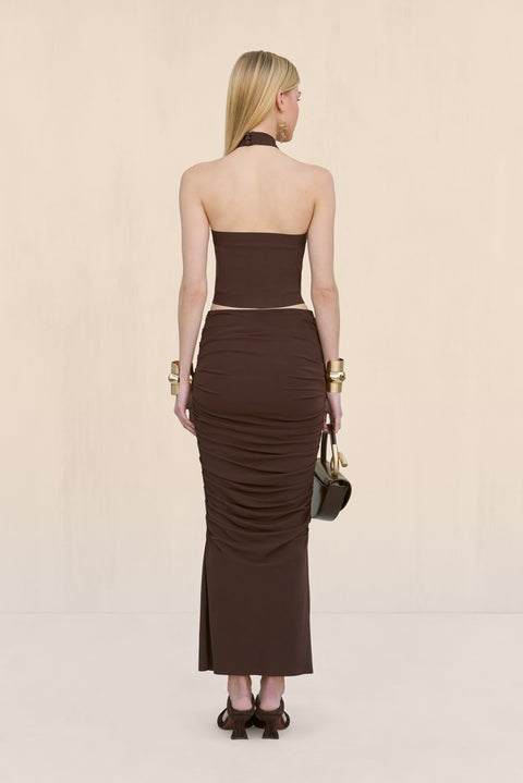 Back-facing woman wearing a brown knit tank top that features a halter neck and open back, paired with a brown maxi skirt. 