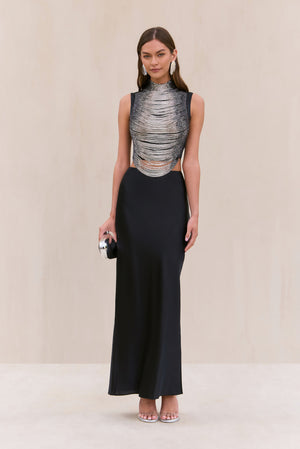 Woman wearing a black silk maxi skirt paired with a tank top that features black and silver ombre beaded strings draping across the bodice. 