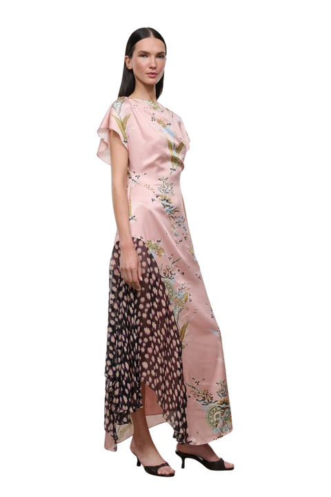 A model wearing a long, high-low dress with a light pink satin top half featuring delicate floral prints, and a sheer, patterned bottom half in black and pink, styled with black heeled sandals against a white background.