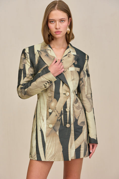 Close up of a woman wearing an oversized double-breasted blazer dress that features a black and tan portrait pattern and fabric covered buttons, paired with chunky gold earrings. 
