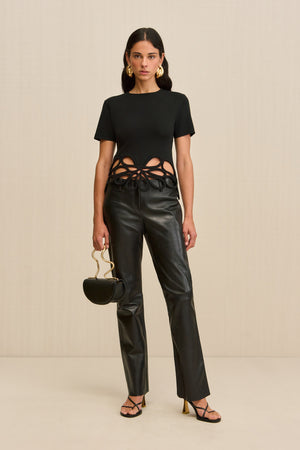 Woman wearing a black, knit t-shirt that features floral cutouts at the bottom hem, paired with black pants and black accessories. 