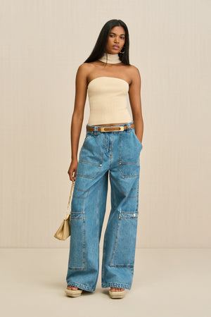Woman wearing a tan knit tube top with a choker detail, paired with blue wide leg jeans. 