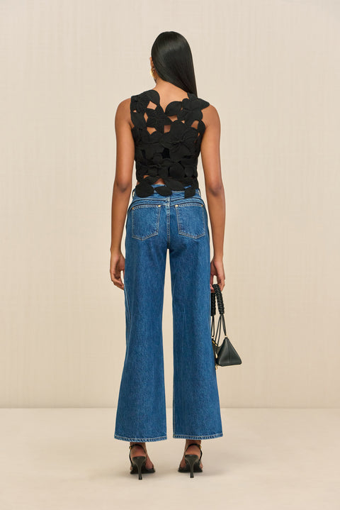 Back-facing woman wearing a black sleeveless crop top that is made of crochet floral appliques. 