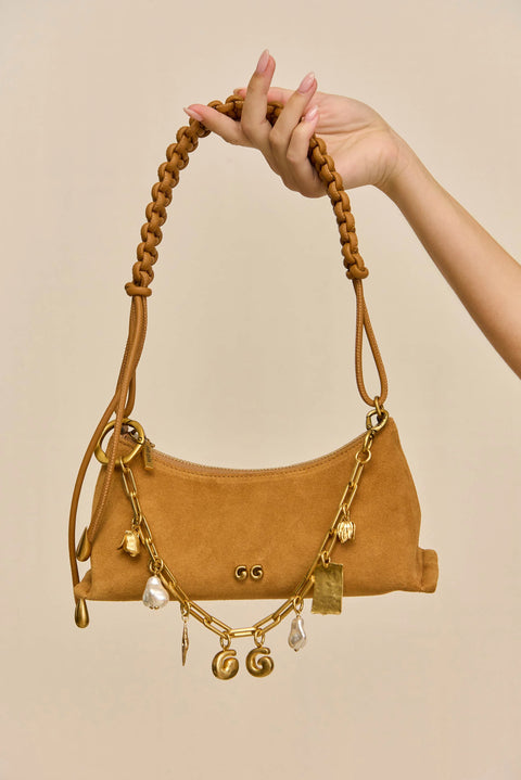 Gold bag chain with various charms on a light beige background with model holding it up