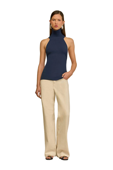 Woman wearing a navy sleeveless top and beige pants on a beige background