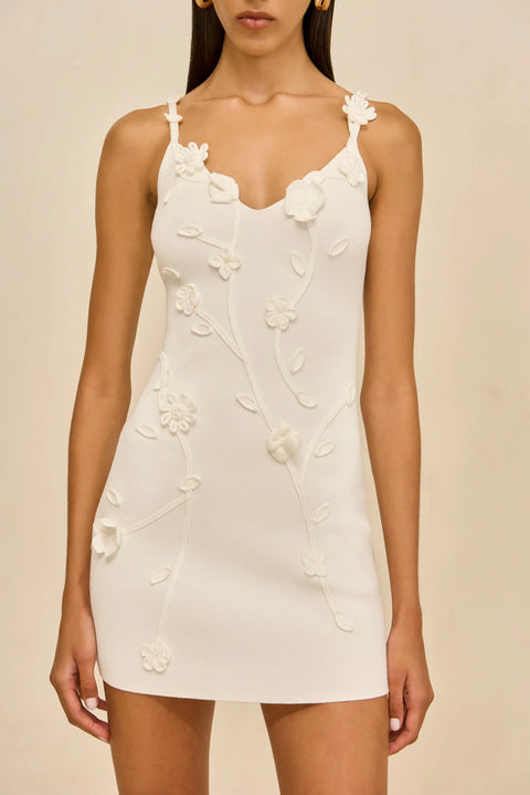 Detail shot of woman wearing a white dress with floral adornments against a beige background