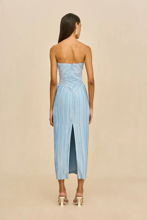 Back-facing shot of woman wearing a light blue strapless pleated dress against a beige background.