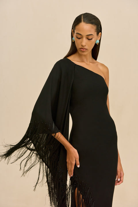 Detail shot of woman wearing a black one-shoulder dress with fringe details on a beige background