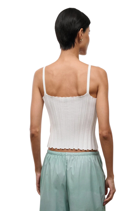 Woman wearing a white ribbed tank top and light green pants on a white background back angle
