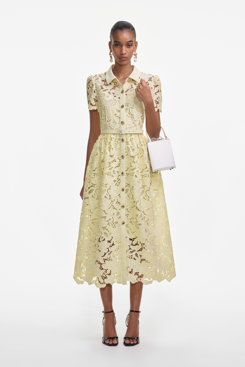 Woman wears yellow lace midi dress with gold buttons and white handbag.