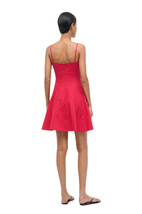 A woman viewed from the back wearing a bright red spaghetti-strap mini dress with a gathered bodice and flared skirt, paired with dark flat sandals, against a plain white background.