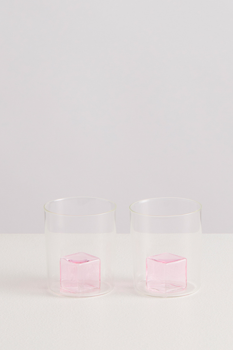 Two transparent glasses with pink glass ice cubes inside on a light gray background