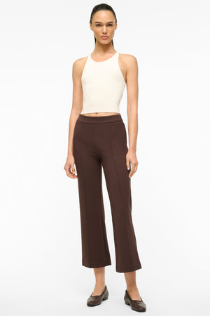 Woman wearing cropped brown pants with a seam down the front of both legs, paired with a white tank.  