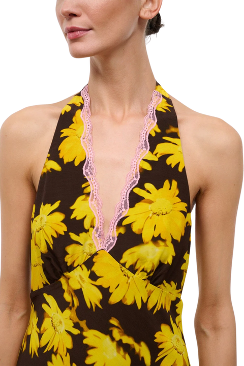 A close-up of a model wearing a halter-neck dress with a brown background, large yellow flower print, and a pink scalloped lace trim along the neckline.
