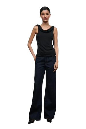 A model wearing a black sleeveless cowl-neck top and dark blue wide-leg trousers, standing against a plain white background.