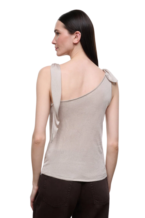 A woman shown from the back wearing a champagne one-shoulder knit top with a tie detail on the shoulder, paired with dark brown pants, against a plain white background.