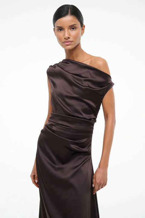Close up of a woman wearing an asymmetrical brown silk midi dress with an off the shoulder design and ruched draping throughout. 
