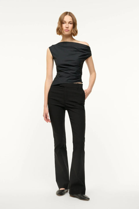 Woman wearing a black off-the-shoulder top that features asymmetrical ruching and hem, paired with black pants. 