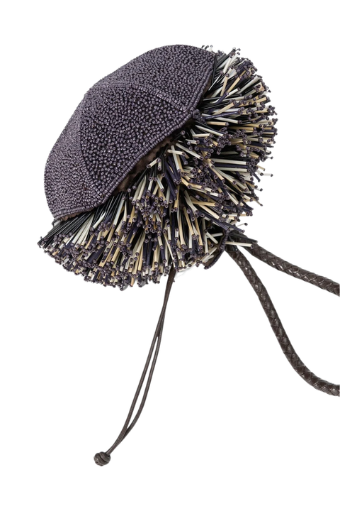 A unique dark gray textured bag featuring a dense, voluminous fringe of black, white, and beige tassels around the brim, with two long dark drawstrings hanging from the back, shown on a plain white background.