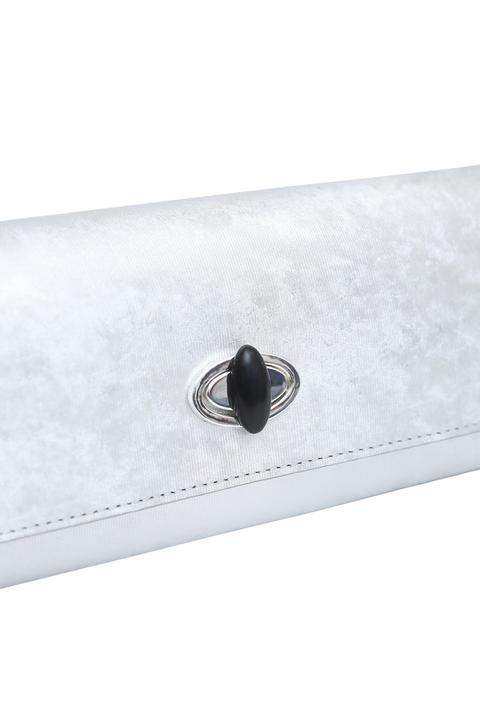 A close-up of a silver textured clutch with a black oval clasp and silver-tone metal ring detail, shown against a plain white background.