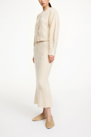 Person wearing a beige cardigan and matching midi skirt on a white background