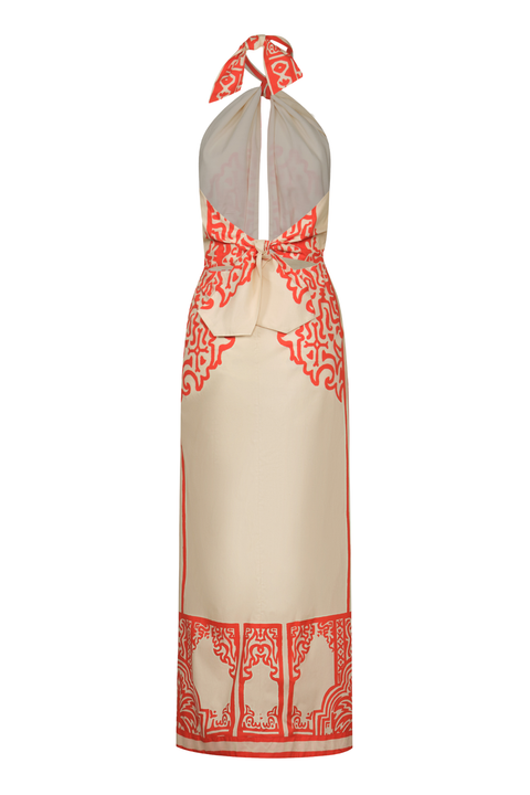 A cream-colored halter-neck maxi dress with a red-orange ornate pattern along the sides, waist, and bottom hem, featuring a tie-neck detail.