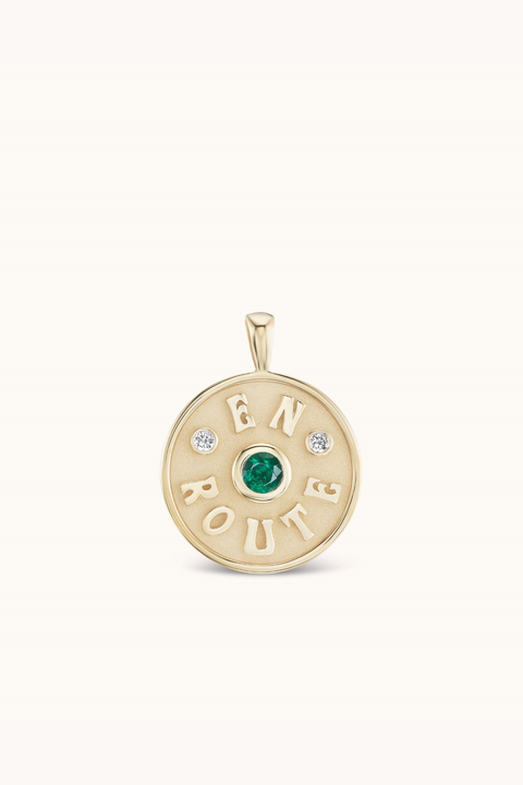 Yellow gold coin charm with raised 'En Route', emerald in center and two small diamonds.