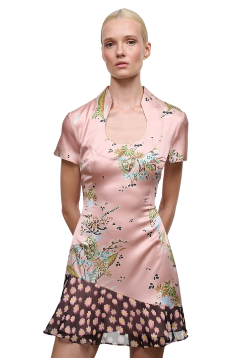 A model wearing a short-sleeved pink satin dress with a floral print and a contrasting black patterned hem, shot against a plain white background.