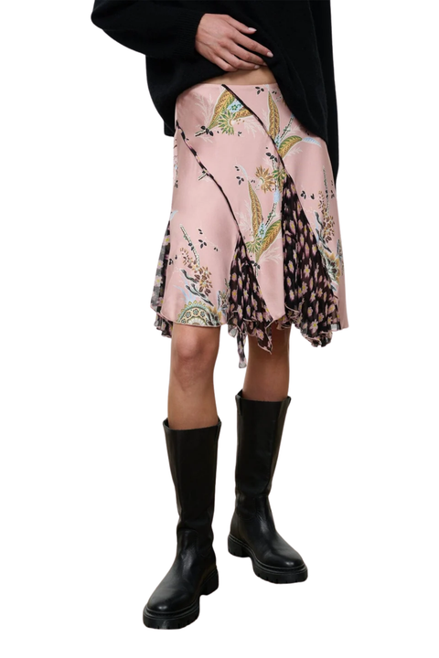 A model is shown from the waist down wearing a light pink skirt with a mixed botanical print pattern, styled with a black top and black knee-high boots against a white background.