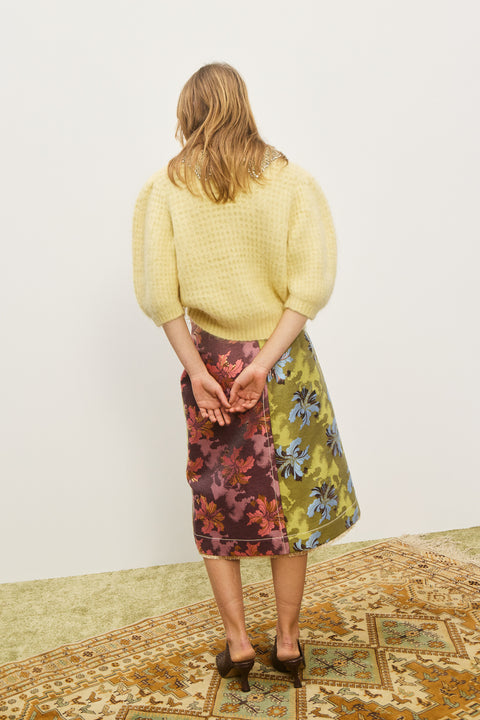 Back-facing woman wearing a yellow sweater with short, puff sleeves and an embellished collar, paired with a patterned skirt. 