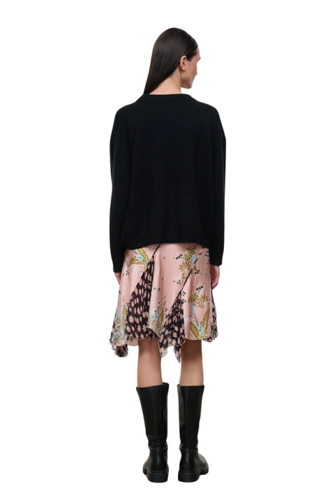 A model shown from the back wearing a black knit sweater, a pink patterned skirt, and black knee-high boots against a plain white background.