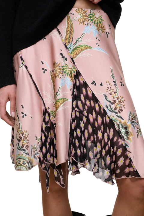 A close-up of a model wearing a pink skirt with a mixed print design, featuring floral patterns.