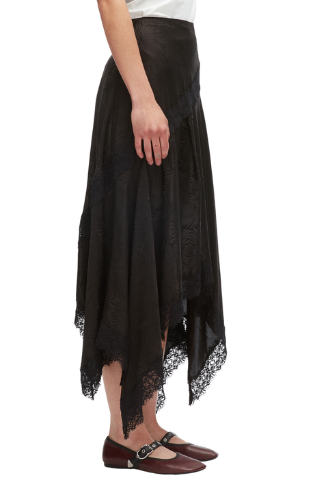 Close up side view of a model wearing a white shirt and black floral jacquard handkerchief skirt. 