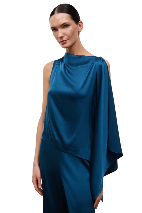A woman modeling a draped satin top and matching trousers in a deep teal blue color, set against a plain white background.