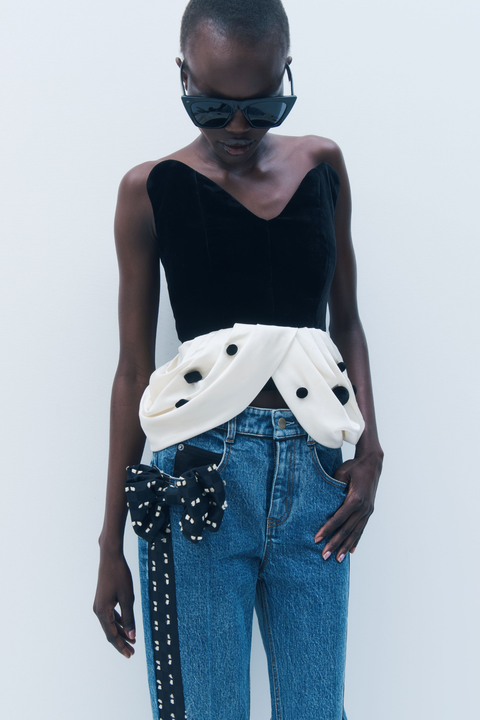 Person wearing a black bustier top, with white peplum hem and blue jeans with a white background