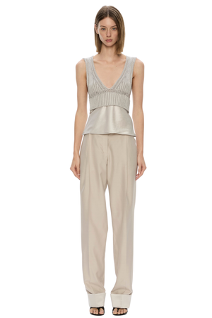 A model wearing a light beige two-piece outfit consisting of a sleeveless ribbed knit top with a deep V-neck and matching wide-leg trousers, photographed against a solid white background.