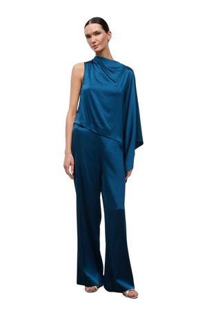 A model wearing a satin-like teal blue one-shoulder draped top and matching wide-leg trousers, shown against a plain white background.