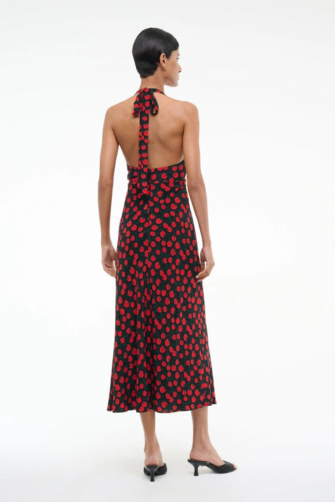 Back view of a woman wearing a black and red tomato print midi dress that features an adjustable tie haler neck and open back, paired with black heels. 