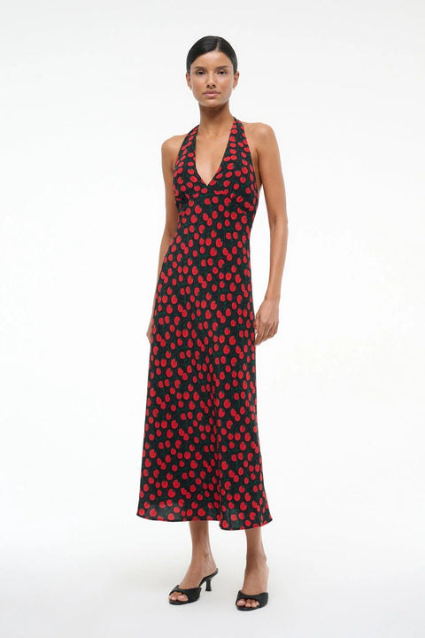 Woman wearing a black and red tomato print midi dress that features a halter neck and deep V, paired with black heels. 