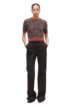 A model stands against a white background wearing a short-sleeve knit cardigan with a red, green, and black tiger print pattern, paired with black wide-leg trousers.