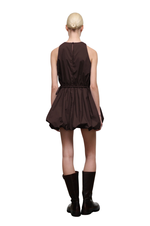 A model shown from the back wearing a sleeveless dark brown mini dress with a gathered waist and puffy skirt, paired with dark brown knee-high boots, against a solid white background.