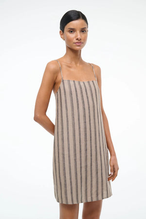 Close up of a woman wearing a mini shift dress with spaghetti straps, crafted from a brown striped linen.