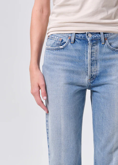 Person wearing light blue mid-rise, straight-leg jeans and a beige top on a white background zoomed in 