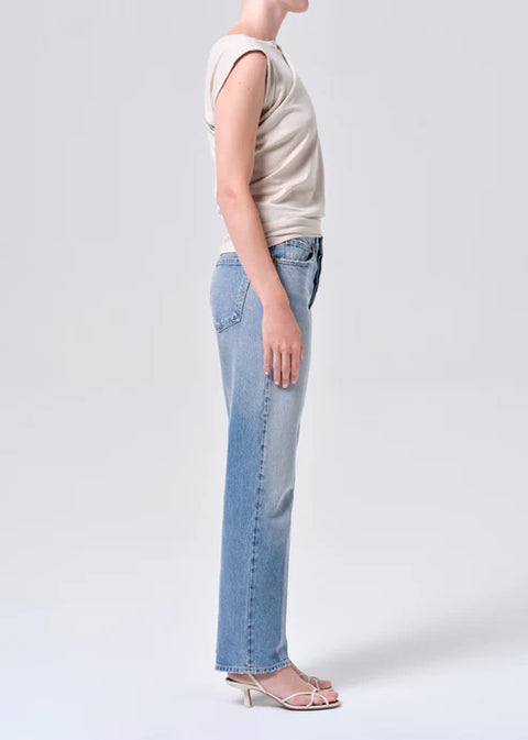 Person wearing light blue mid-rise, straight-leg jeans and a beige top on a white background from the side