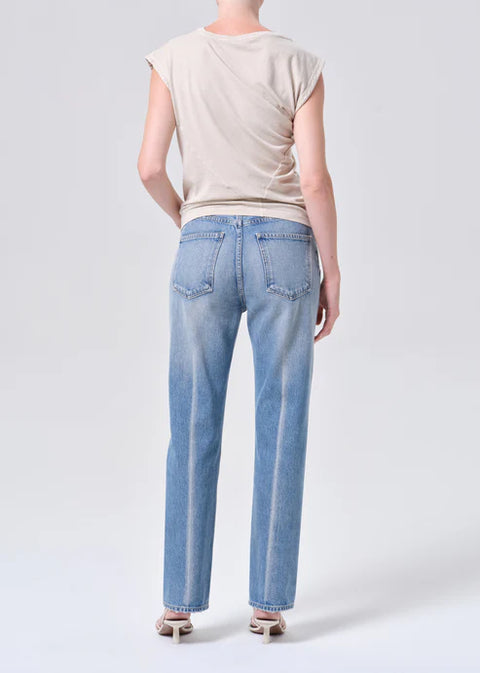 Person wearing light blue mid-rise, straight-leg jeans and a beige top on a white background from the back 