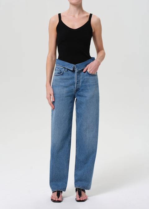 Woman wears blue jeans with fold over at waist and black tank top.