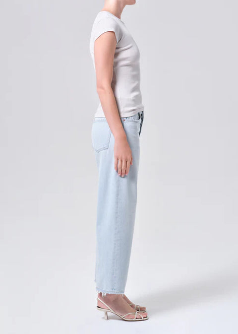 Person wearing mid-rise, wide-leg, light blue jeans and a white t-shirt on a plain background from the side