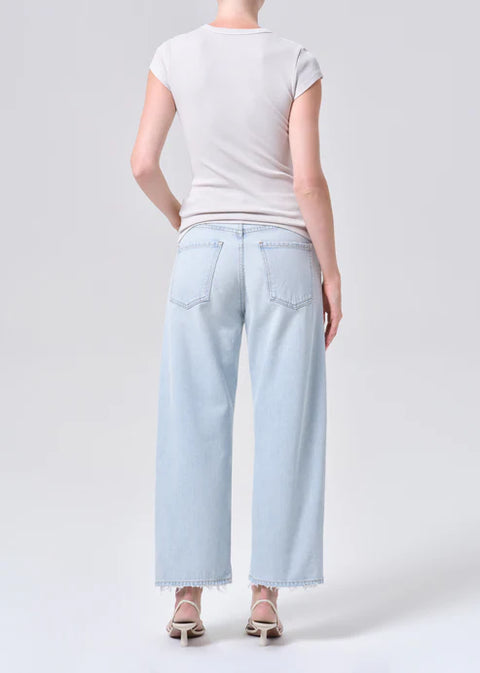 Person wearing mid-rise, wide-leg, light blue jeans and a white t-shirt on a plain background from the back